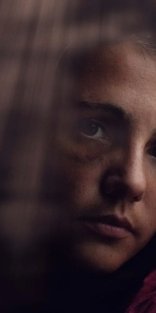 Close-up do rosto de uma pessoa com expressão de profunda tristeza e angústia em ambiente escuro.